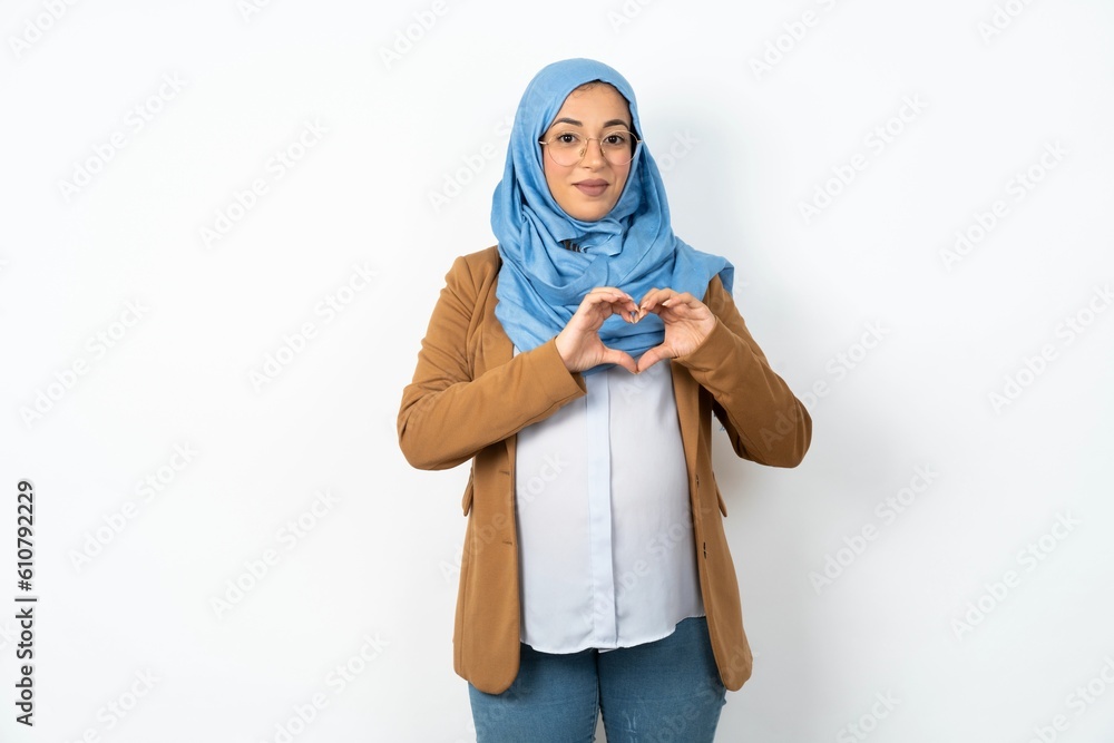 Serious Young beautiful pregnant muslim woman wearing hijab over white background keeps hands crossed stands in thoughtful pose concentrated somewhere