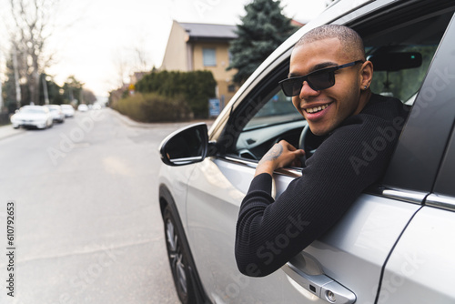 Afro-American man looks from the luxury car window and smiles while driving car. High quality photo © PoppyPix