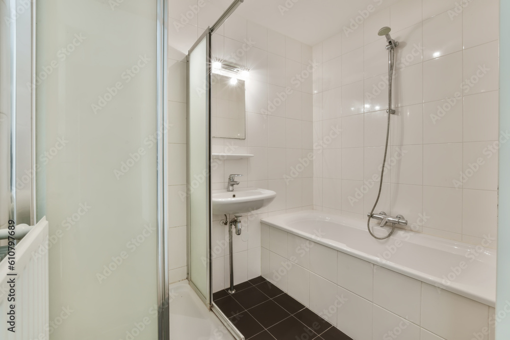 a white bathroom with black tile flooring and wall to wall glass shower stall door in the bathtub is next to the sink a white bathroom with black tile flooring and wall to wall glass shower stall door in the bathtub is next to the sink