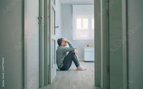 Desperate man with mental disorder and suicidal thoughts holding his head with hand sitting on the room floor of a mental health center