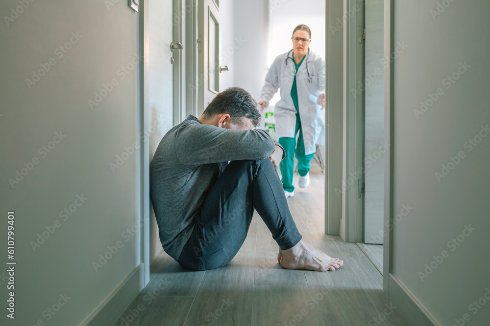 Worried female doctor running to help male patient with mental disorder and suicidal thoughts crying sitting on the floor of hallway Worried female doctor running to help male patient with mental disorder and suicidal thoughts crying sitting on the floor of hallway