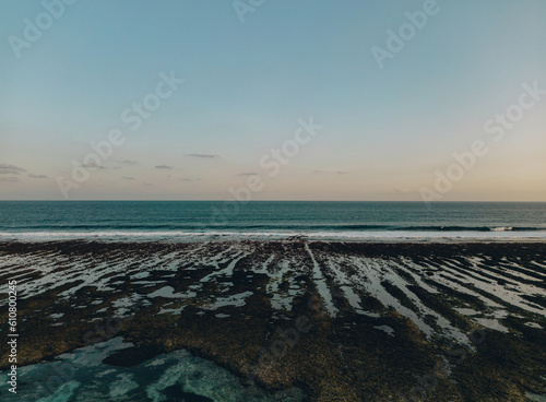 Sunset stone serene beach with clear blue water and shoreline. Waves crash against the beach
