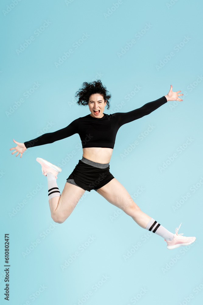 Overjoyed dark haired woman wearing sportive clothes jumping high looking at camera