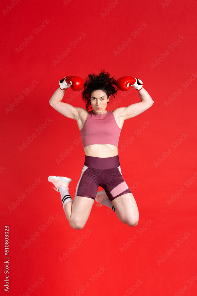 Concentrated young sports woman boxer wearing red boxing gloves, jumping high up