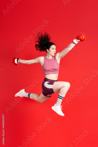 Full size of young sports woman boxer wearing red boxing gloves, making direct hit