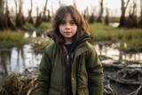 Portrait of a beautiful little girl in a green jacket on the background of the river