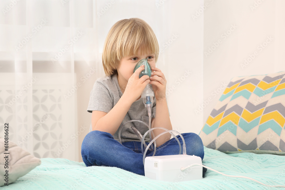 Sick little boy using nebulizer for inhalation on bed at home