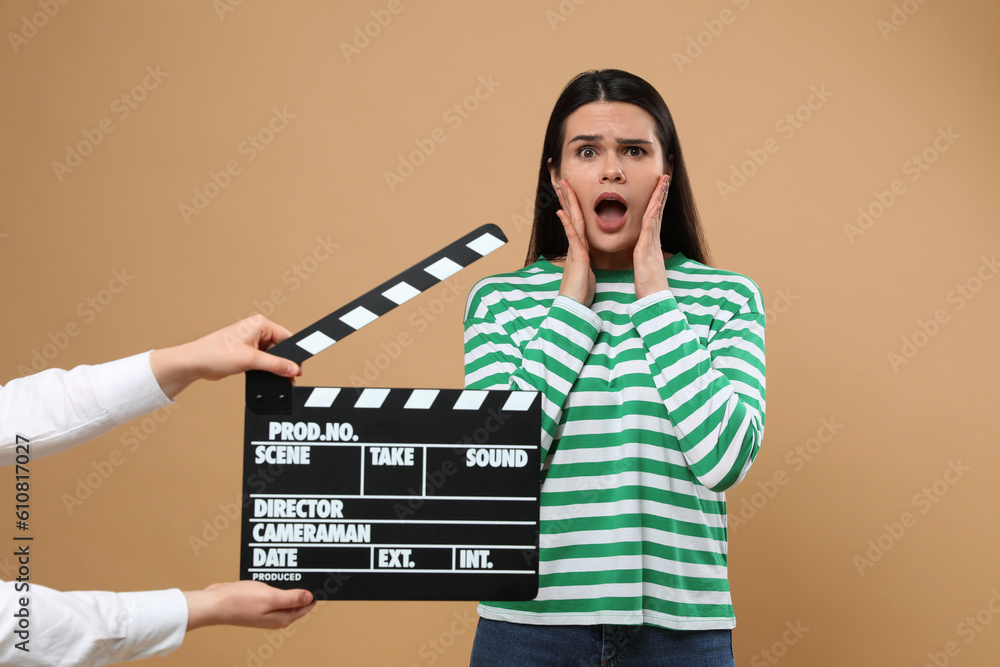 Emotional actress performing while second assistant camera holding clapperboard on beige background. Film industry