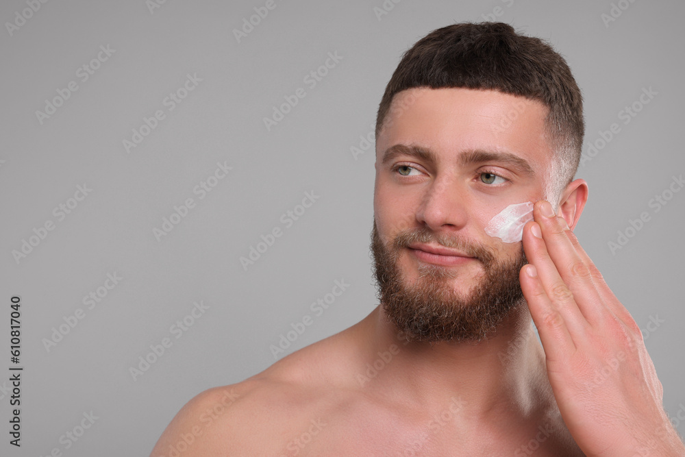 Fototapeta premium Handsome man applying cream onto his face on light grey background, space for text