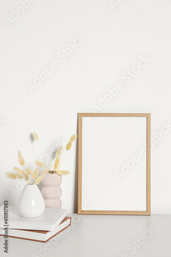 Empty photo frame and vases with dry decorative spikes on white table. Mockup for design
