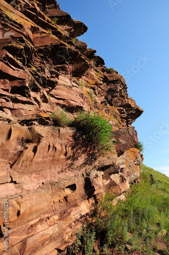 Bushes and grass on layered red sandstone rock formations at the top of a hill.