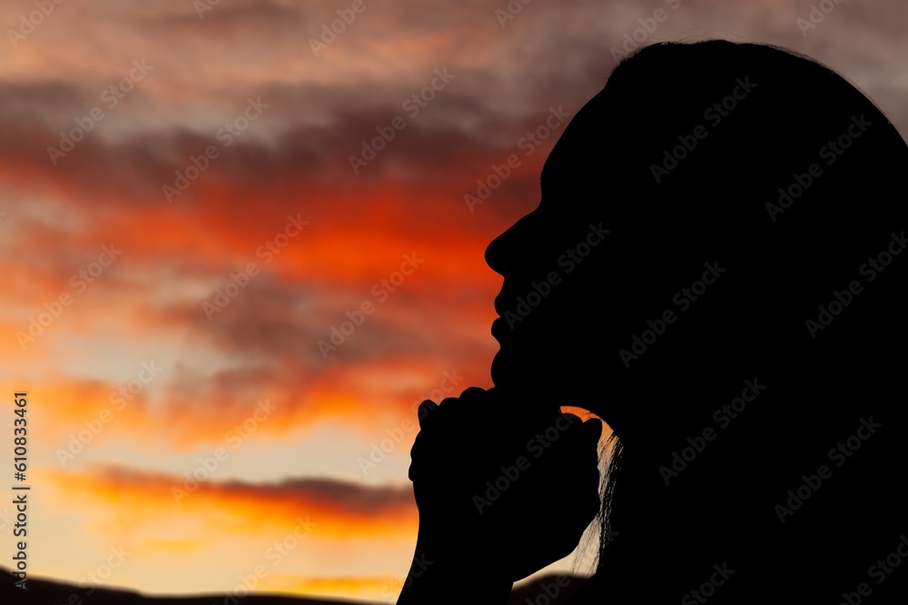 Silhouette of young woman praying to God on sky background.