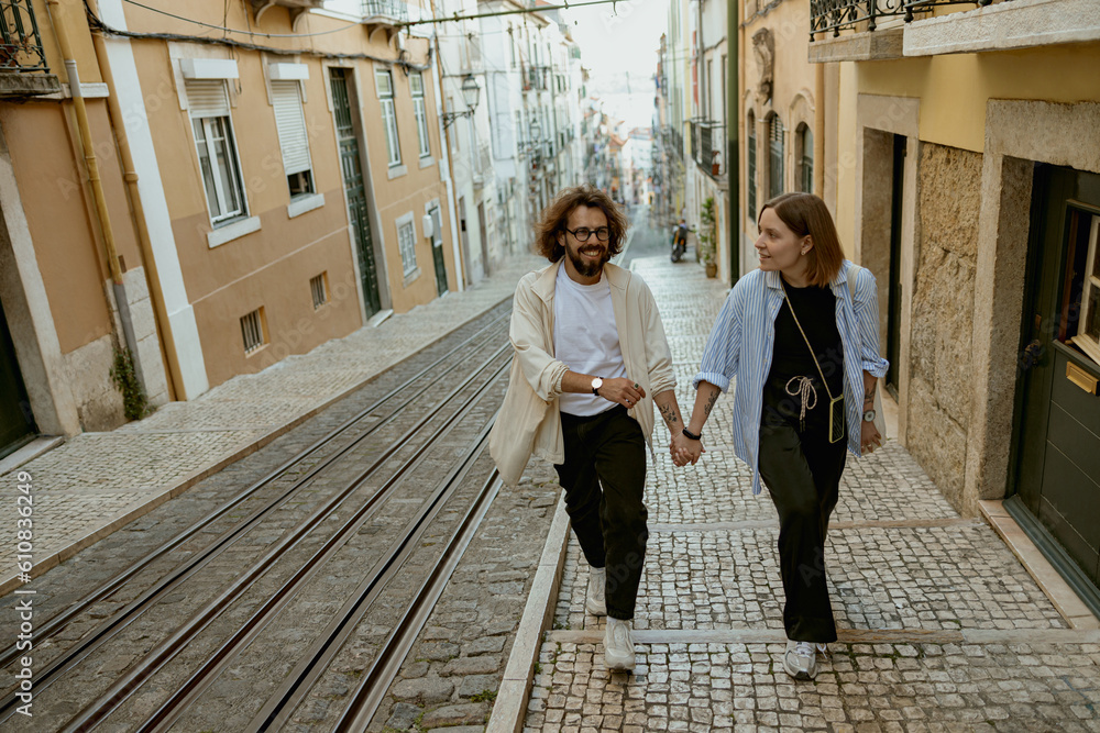Smiling romantic hipster couple in love holding hands while walking on old city street in Lisbon 