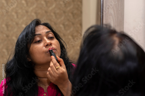 Beautiful Asian woman front of mirror applying make up lips with lipstick at bed room.