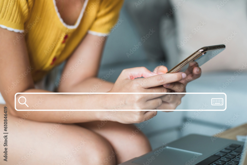 Fototapeta premium Young woman wearing yellow t-shirt sitting on sofa at living room use their smartphones to find out what interests them, to find ideas about networking and online learning with search bar icon.