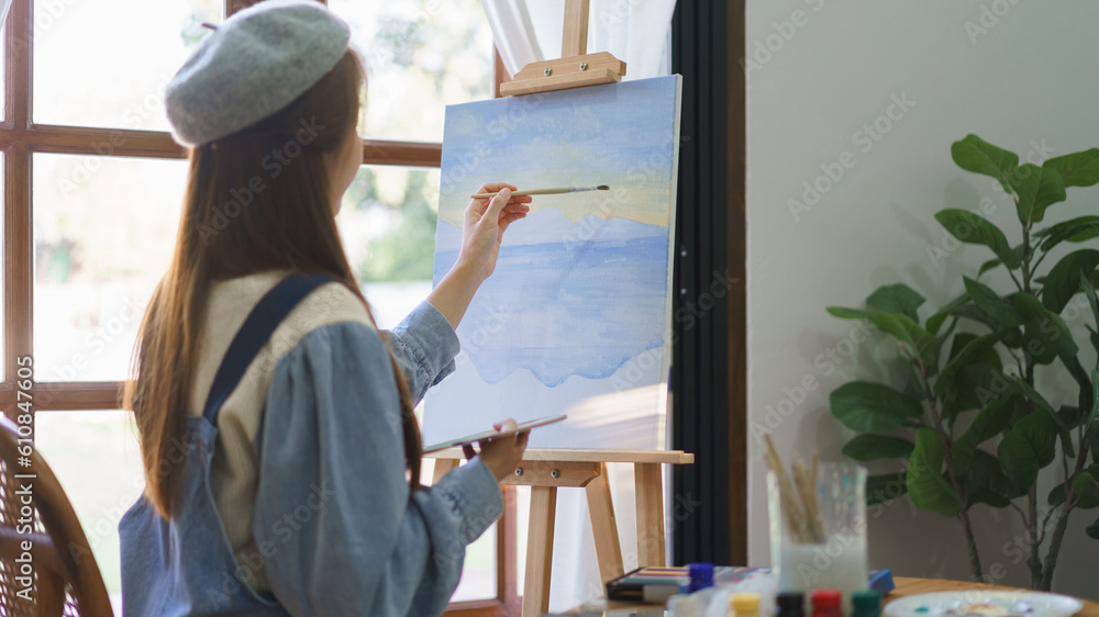 Young female painter using paintbrush to drawing and painting masterpiece on canvas in home studio Young female painter using paintbrush to drawing and painting masterpiece on canvas in home studio