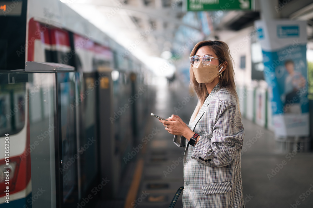 Asian woman business passenger with casual suit using the smart mobile phone in the BTS Skytrain rails or MRT subway for travel in the big city, lifestyle and transportation concept Asian woman business passenger with casual suit using the smart mobile phone in the BTS Skytrain rails or MRT subway for travel in the big city, lifestyle and transportation concept
