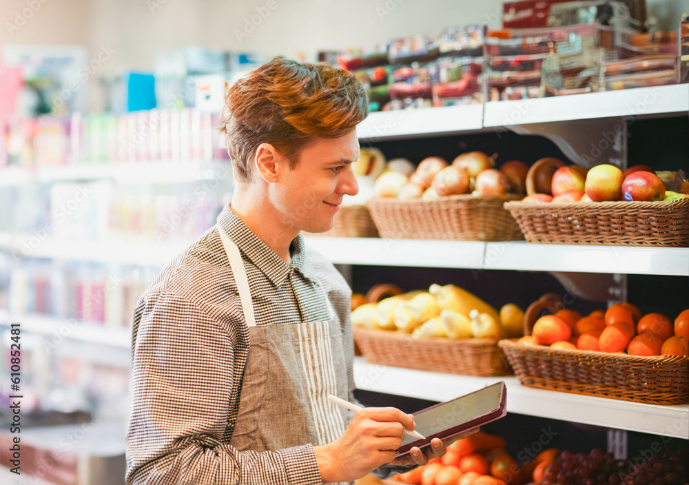 Candid Lifestyle young staff man in fresh mart fruit store checking quality of product on the shelve with tablet. Young male without mask working in minimart.