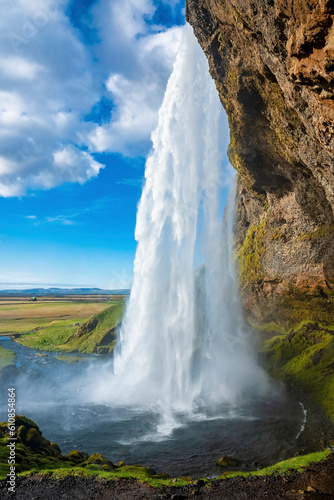 Close-up of Seljalandsfoss flowing from mountain against cloudy blue sky