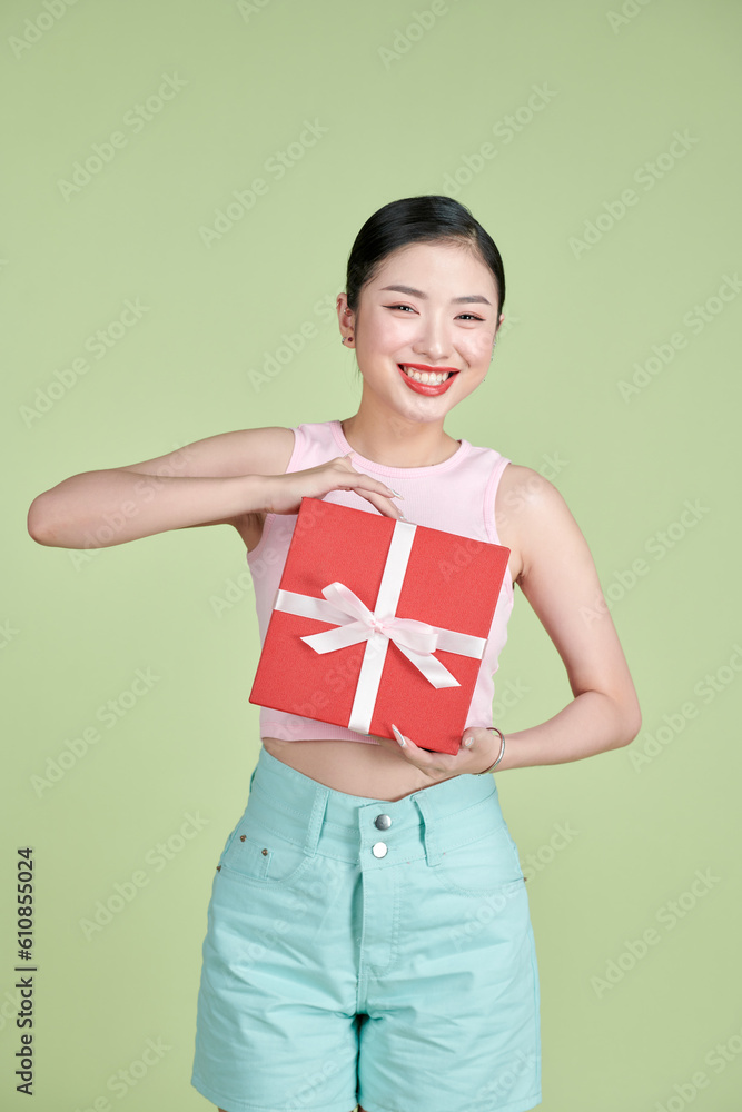 Happy pretty young woman holding gift box over green background Happy pretty young woman holding gift box over green background
