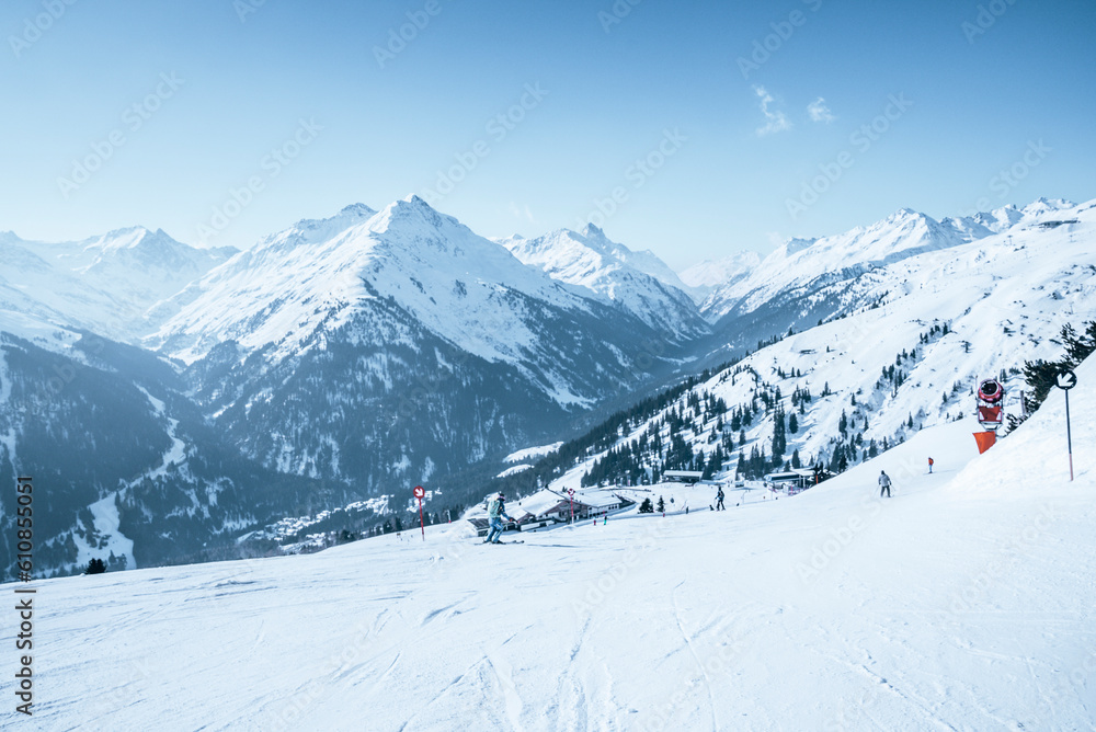 Skiers skiing on snow covered mountain slope against blue sky