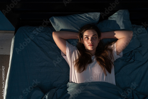 Stressed young woman on bed at night suffering from insomnia, top view. Depressed awake girl lying in bed and looking above late