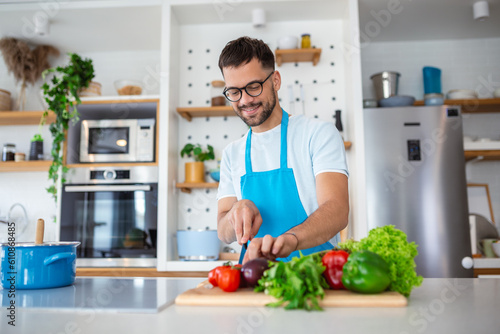 Handsome young man man stand at modern kitchen chop vegetables prepare fresh vegetable salad for dinner or lunch, young male cooking at home make breakfast follow healthy diet, vegetarian concept