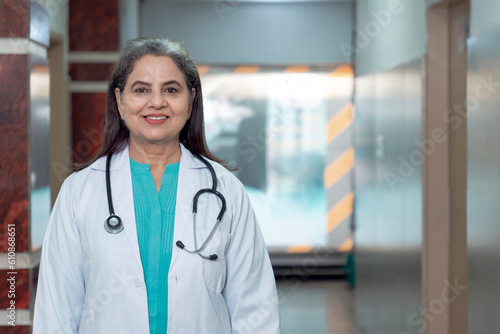 Medical concept, Indian senior female doctor in white coat with stethoscope standing at hospital.