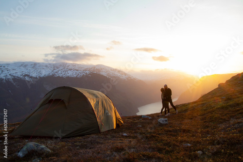 Couple hugging in sunset by their tent, looking out over the fjord. photo