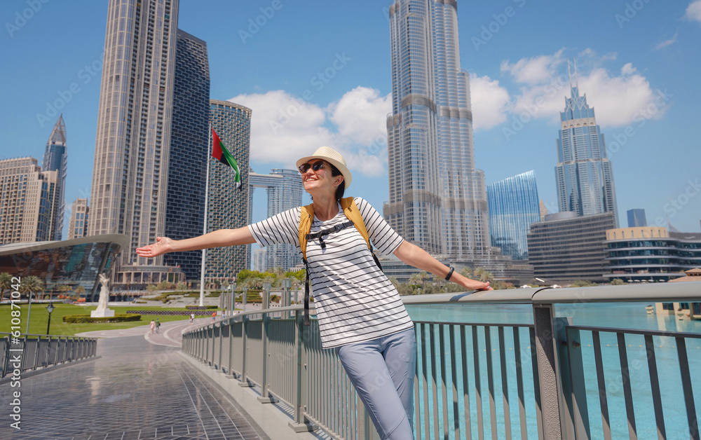 Enjoying travel in United Arabian Emirates. Young woman with yellow backpack walking on Dubai Downtown in sunny summer day.