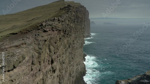 Dramatic Nature Scenic Of A Person In Distance Hiking At The Traelanipa Cliff Towering Above The Atlantic Coast In Vagar, Faroe Islands In Denmark. tilt-up photo