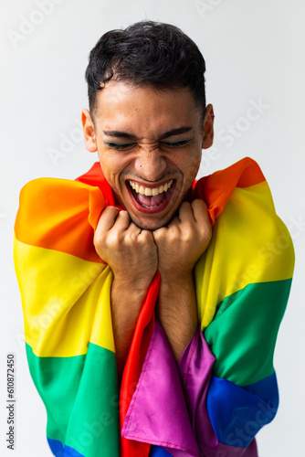 Happy biracial transgender man holding rainbow flag with eyes closed on white background