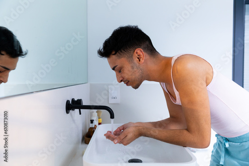 Biracial transgender man washing face in bathroom