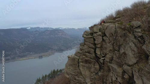A boyfriend and a girlfriend couple sitting on the edge of a steep cliff enjoying a beautiful and scenic view out in the nature. Angels Rest, Oregon USA - circa 2023.