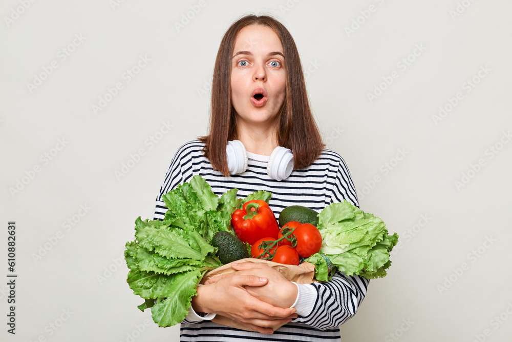 Healthy beating. Useful food. Astonished surprised woman embraces fresh vegetables looking at camera with open mouth posing isolated over white background. Healthy beating. Useful food. Astonished surprised woman embraces fresh vegetables looking at camera with open mouth posing isolated over white background.