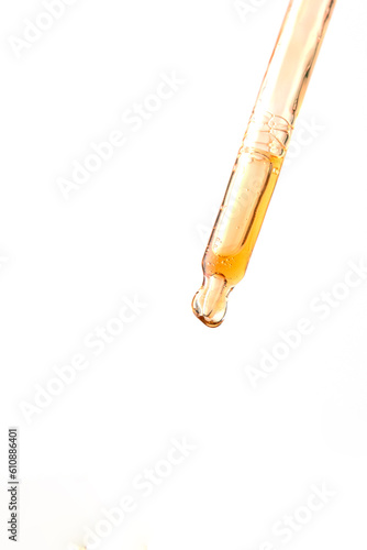 Cosmetic pipette with yellow liquid drop at isolated white background