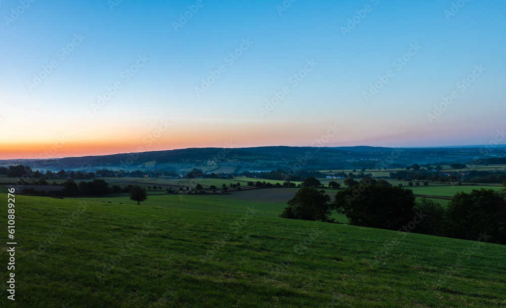 An early morning with a sky full of beautiful colors during sunrise in the rolling hills landscape of Limburg with spectacular views over the typical small villages of this region