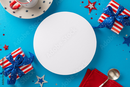 Set stage for unforgettable USA-themed celebration. Top view of table arrangement featuring tableware, spoon, cup, napkin, star decor, confetti, gifts. Blue backdrop with empty circle for text or ad