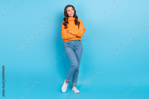 Full length photo of excited dreamy woman wear orange sweater looking emtpy space arms folded isolated blue color background