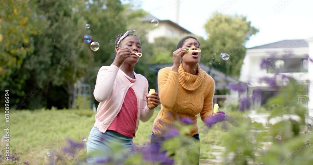 Happy african american daughter and mother blowing bubbles in sunny garden Happy african american daughter and mother blowing bubbles in sunny garden