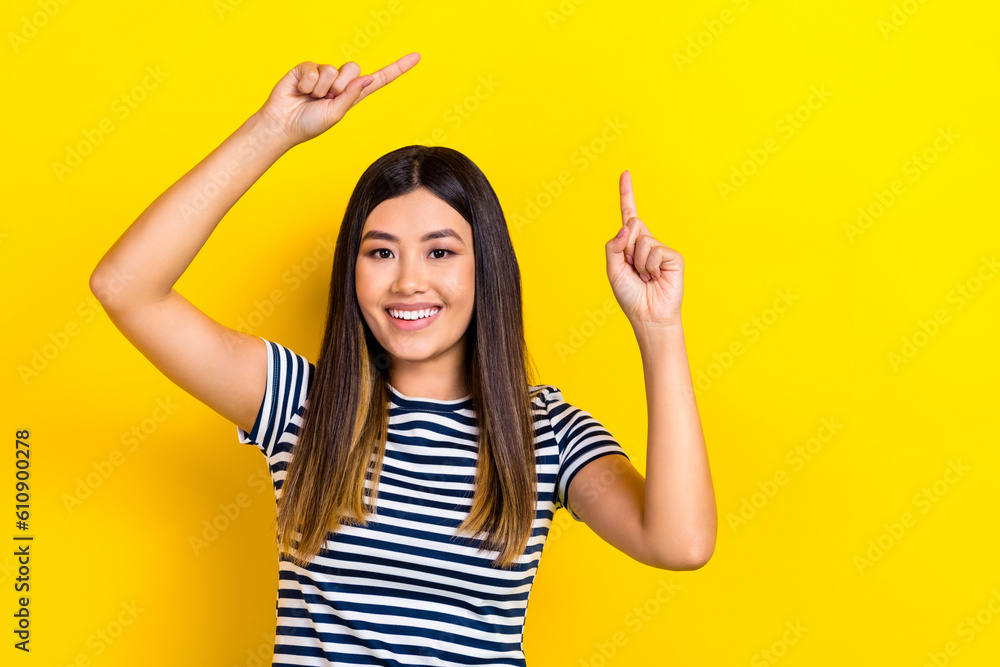Photo of young beautiful girl black hair wear striped t-shirt directing finger empty space ad promo isolated on yellow color background Photo of young beautiful girl black hair wear striped t-shirt directing finger empty space ad promo isolated on yellow color background