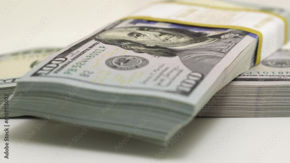 stack of bank bundles with US dollars on a white background. Close-up shot of new, freshly printed hundred-dollar bills rotating on a table. cash flow, business investment, or big money concepts.