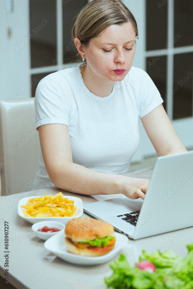 Woman eating unhealthy lunch while studying online courses in the kitchen. Remote work, a freelancer working at home and eating junk food.