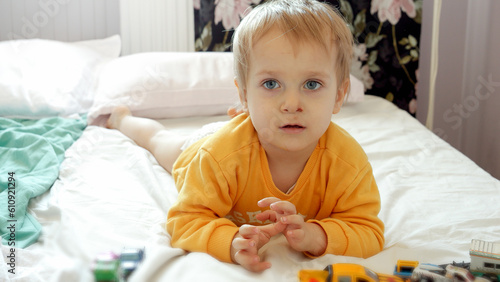 Cute funny boy with dirty face lying on bed and playing with colorful cars. Child development, education and entertainment
