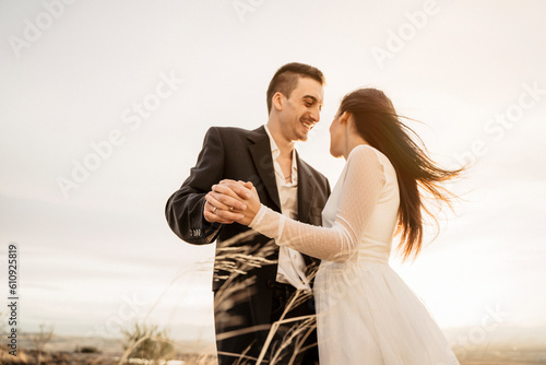 Pareja joven de novios recien casados celebrando su boda informal con una sesion de fotos al atardecer en el campo, el novio enamorado la mira sonriente photo