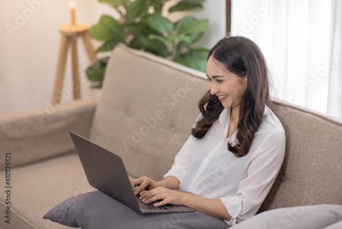 Portrait of a young happy asian female freelancer sitting on the couch and working on project, watching movie on laptop, studying, blogging, resting and chatting online.