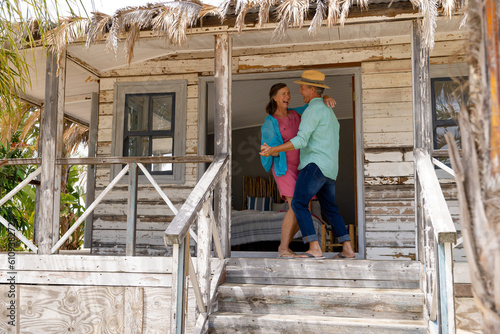 Happy caucasian senior husband and wife dancing cheerfully on balcony outside wooden cottage