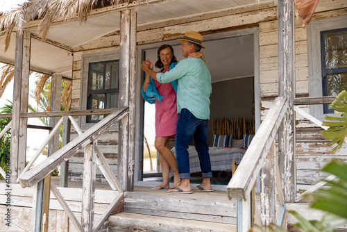 Happy caucasian senior couple wife dancing cheerfully on balcony outside wooden cottage