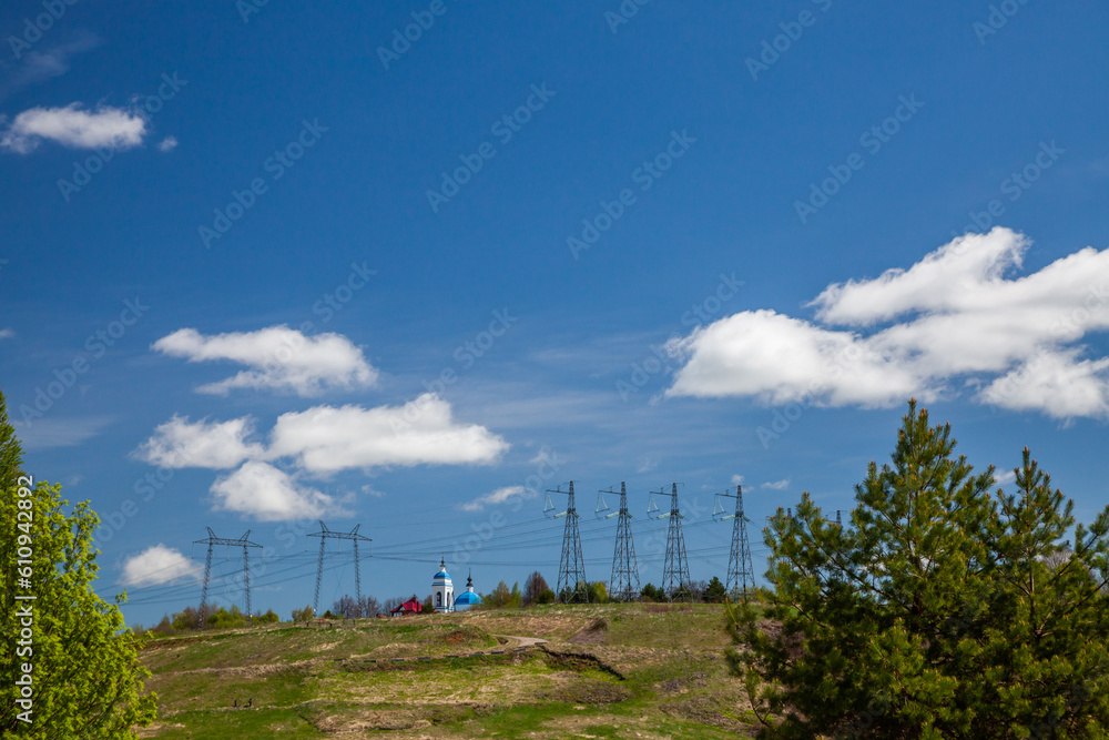 Summer landscape with church and electric power line against blue sky and clouds