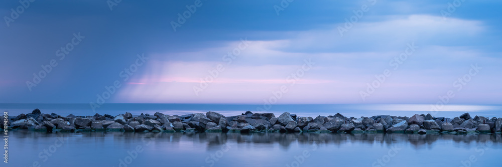 Breakwater built of stones. Long exposure photo. The Baltic Sea just before the storm.